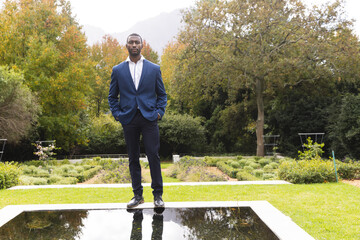 Obraz premium Thoughtful african american groom standing by pond in sunny garden, copy space