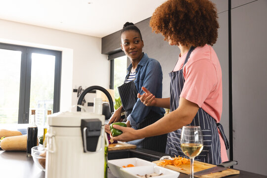 Happy diverse couple preparing meal, washing vegetables and talking in kitchen