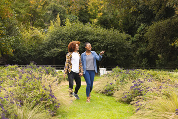 Happy diverse couple holding hands, walking in garden and pointing