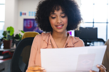 Biracial woman reading a document during a video call at office - Powered by Adobe