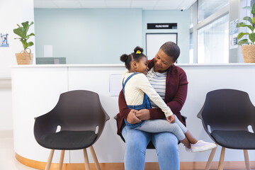 Happy african american mother and daughter sitting in waiting room at hospital, copy space - Powered by Adobe