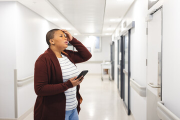 Worried african american female patient using smartphone in waiting room at hospital, copy space