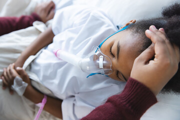 Fototapeta premium African american girl patient lying on bed with oxygen mask, with her mother at hospital