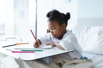 African american girl patient lying on bed colouring in patient room at hospital