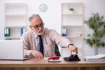 Old male employee speaking by phone at workplace