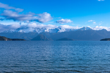 Photograph of a large blue lake and snow-capped mountain range while driving from Te Anau in Fiordland to Manapouri on the South Island of New Zealand