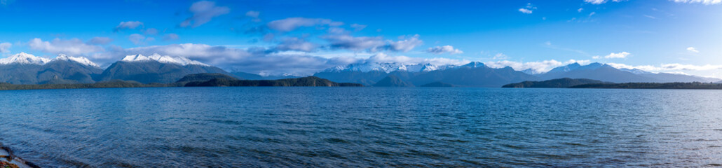 Photograph of a large blue lake and snow-capped mountain range while driving from Te Anau in Fiordland to Manapouri on the South Island of New Zealand - obrazy, fototapety, plakaty
