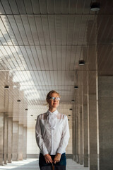 A young beautiful blonde teacher or student in a white shirt and glasses on the background of a school or university building