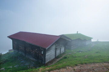 Fototapeta na wymiar Highland landscape in cloudy and foggy weather. Highland houses made of stone and wood. Wooden plateau houses built on the hill. Wooden plateau houses in Turkey. Pokut Plateau Rize Türkiye.