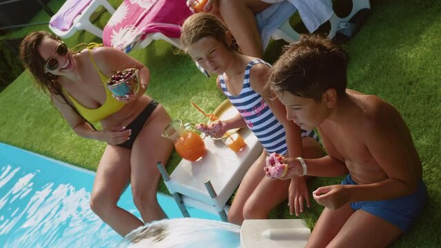 Multi-generational family of happy people enjoying themselves by the pool eating fruit and donuts.