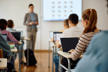 Back view of teenage girl using laptop during computer class at high school.