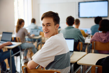 Happy high school student attending computer class in classroom and looking at camera. - obrazy, fototapety, plakaty