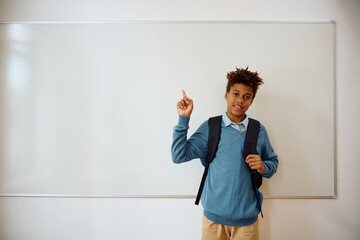 Happy black high school student pointing at whiteboard in classroom.