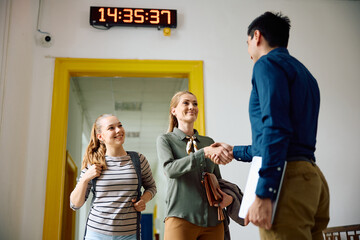 Happy mother of teenager girl shaking hands with high school principal.