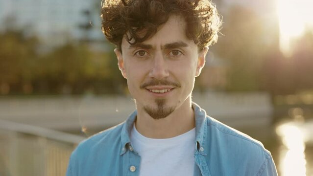Portrait of a young student standing in the park, smiling and looking at camera with beard. Real people concept