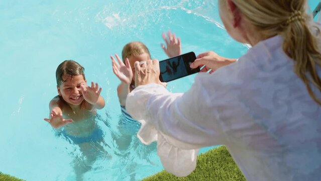 Mature woman grandmother takes pictures of her grandchildren with her phone while they are swimming in the pool on vacation