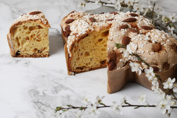 Delicious Italian Easter dove cake (traditional Colomba di Pasqua) and flowers on white marble table, closeup
