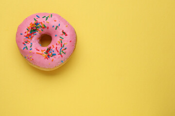 Obraz na płótnie Canvas Tasty glazed donut decorated with sprinkles on yellow background, top view. Space for text