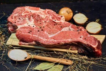 A piece of raw meat and spices lie on a wooden cutting board. Raw food for cooking.