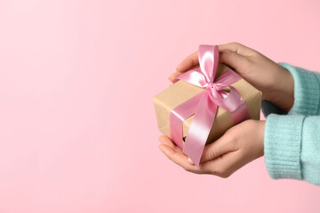Woman holding gift box with bow on pink background, closeup. Space for text