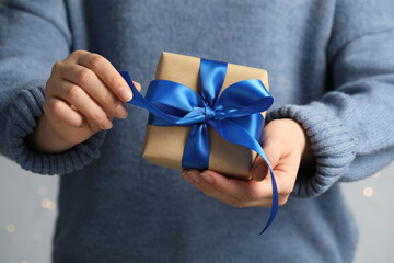Woman holding gift box with blue bow on light grey background, closeup