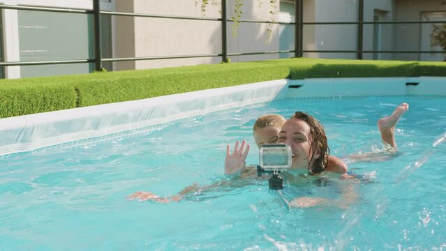 Mom and her little daughter swimming together and playing in the pool using a selfie stick and GoPro camera for fun and filming