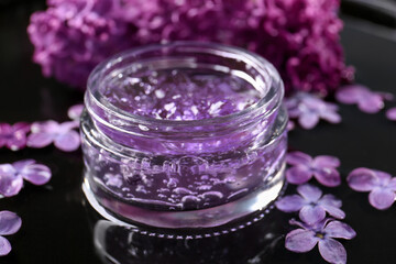 Obraz na płótnie Canvas Jar of cosmetic product and lilac flowers on black surface, closeup