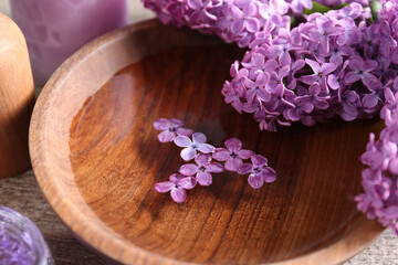 Fototapeta na wymiar Bowl of water and lilac flowers on wooden table, closeup