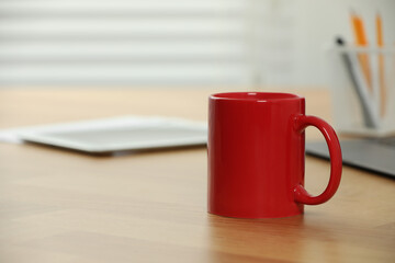 Red ceramic mug on wooden table at workplace. Mockup for design