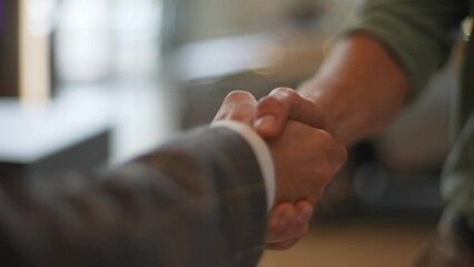 Close-up hands of unrecognizable male dealer and customer shaking hands in front of automobiles in car dealership. Concept of choosing and buying new car at showroom. Shooting in slow motion.
