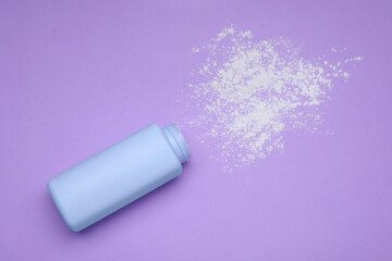 Bottle and scattered dusting powder on violet background, top view. Baby cosmetic product