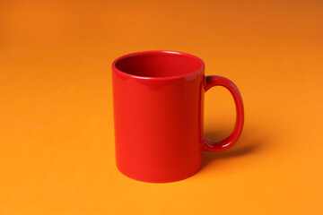 One red ceramic mug on orange background