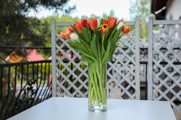 Beautiful colorful tulips in glass vase on white table at balcony