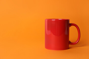 One red ceramic mug on orange background. Space for text