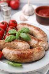 Plate with tasty homemade sausages, basil leaves and tomatoes on table, closeup