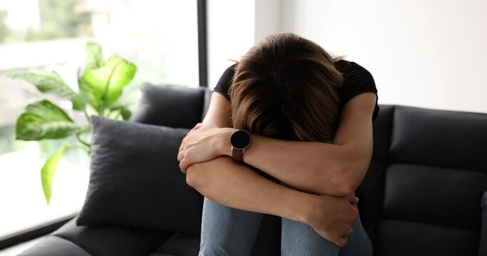 Frustrated woman covering face and crying sitting on sofa at home alone. Upset young woman suffering from boyfriend breakup or divorce