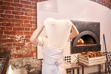 The chef prepare pizza. Raw pizza ready to bake. Cook in a apron in the kitchen Rolls out pizza dough. boxes for food delivery on background.