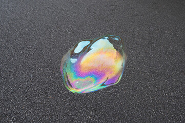 Detail of big colorful soap bubble against black asphalt background. - 627604150