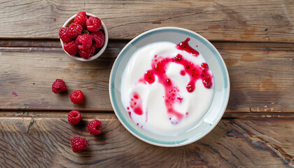 fresh greek yogurt with colored stains of berry juice and whole raspberry, dewberry on plate on old wooden table, view from above