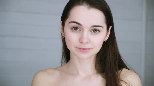 A happy smiling girl with nude make-up looking at camera and dancing. Sexy look. Closeup portrait. A beautiful 30s woman fixes her hair with hands. A winter color type appearance. Seductively winks.