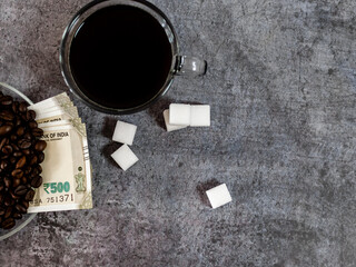Closeup shot of black coffee, sugar cubes and money covered with roasted coffee beans.
