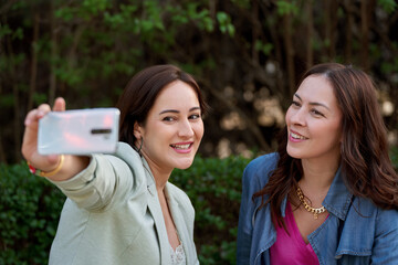 Two women taking a selfie with a mobile phone outdoors. Technology and friendship concept.