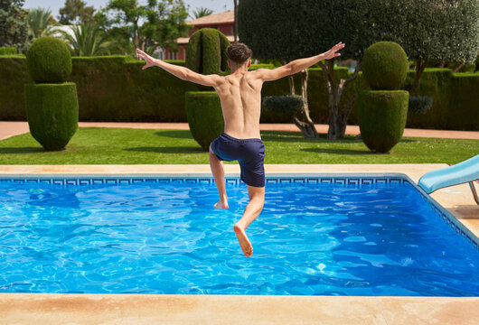 Unrecognizable boy jumping into pool water with trees on poolside