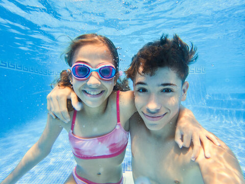 Cheerful boy and girl inside blue clear swimming pool
