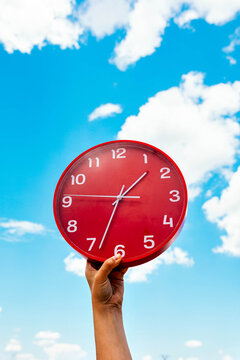 Crop hand with red clock against blue sky