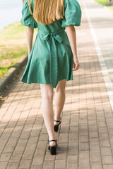 Close-up of women's legs. A girl walks in a green dress in the park in summer.