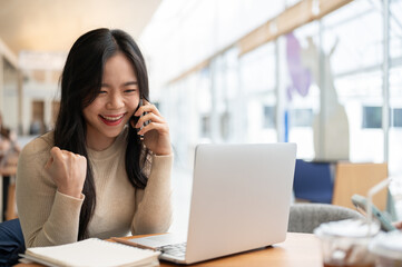 A happy Asian woman rejoicing after receiving good news over the phone while working remotely
