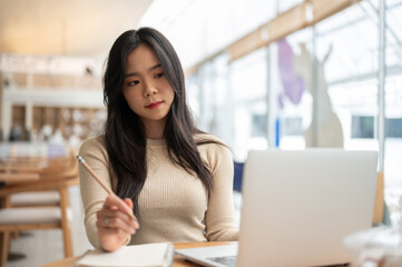 A beautiful and focused Asian woman is looking at her laptop screen with a serious face