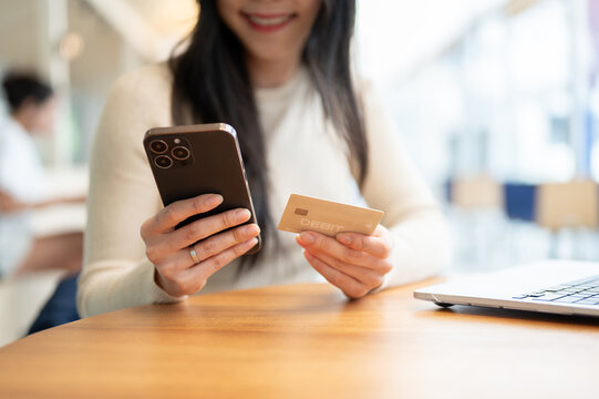 Close-up image of a happy woman using her mobile banking app while sitting at a table