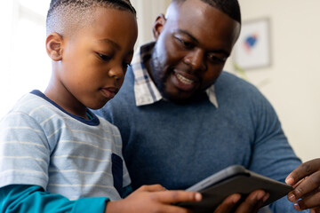 Happy african american father and son sitting in living room at home using tablet together